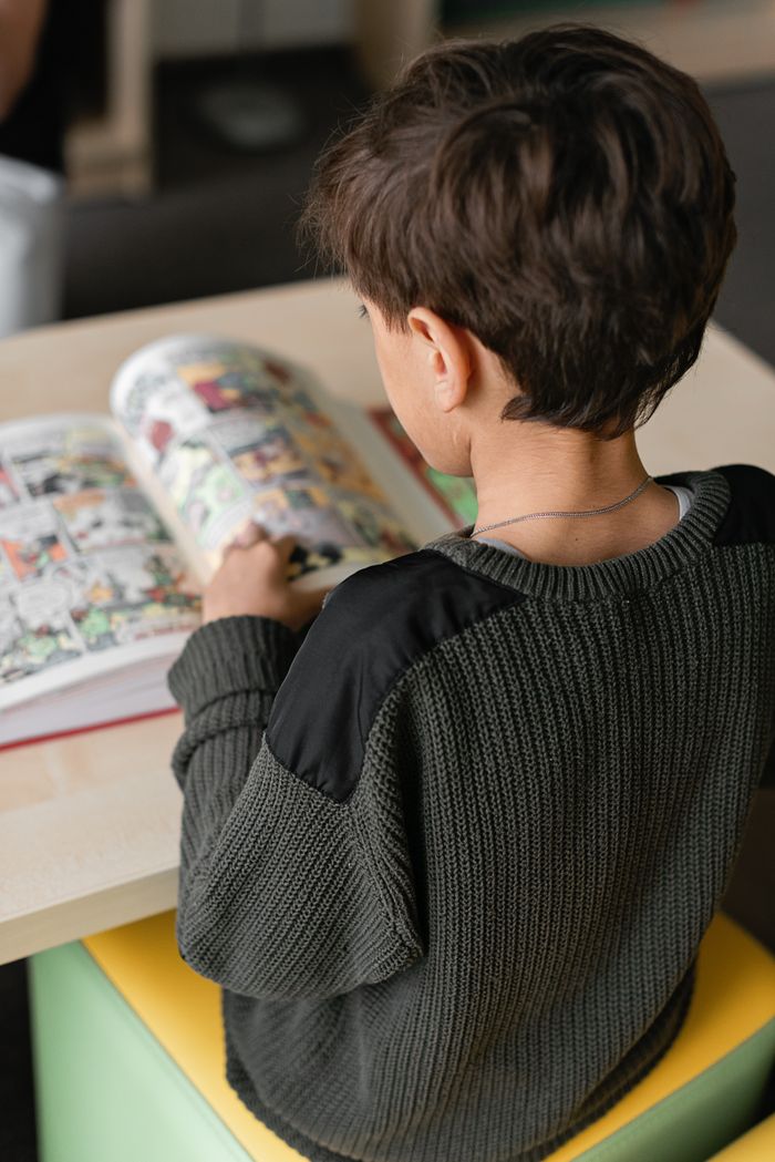 our-story Young boy sitting indoors reading a colorful comic book.